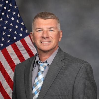 City Manger Tom Ernharth standing in front of an american flag wearing a grey suit jacket